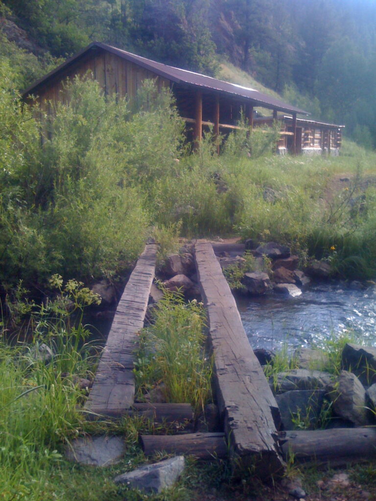 Holzsteg über einen Bach in ruhiger Natur mit Hütte im Hintergrund